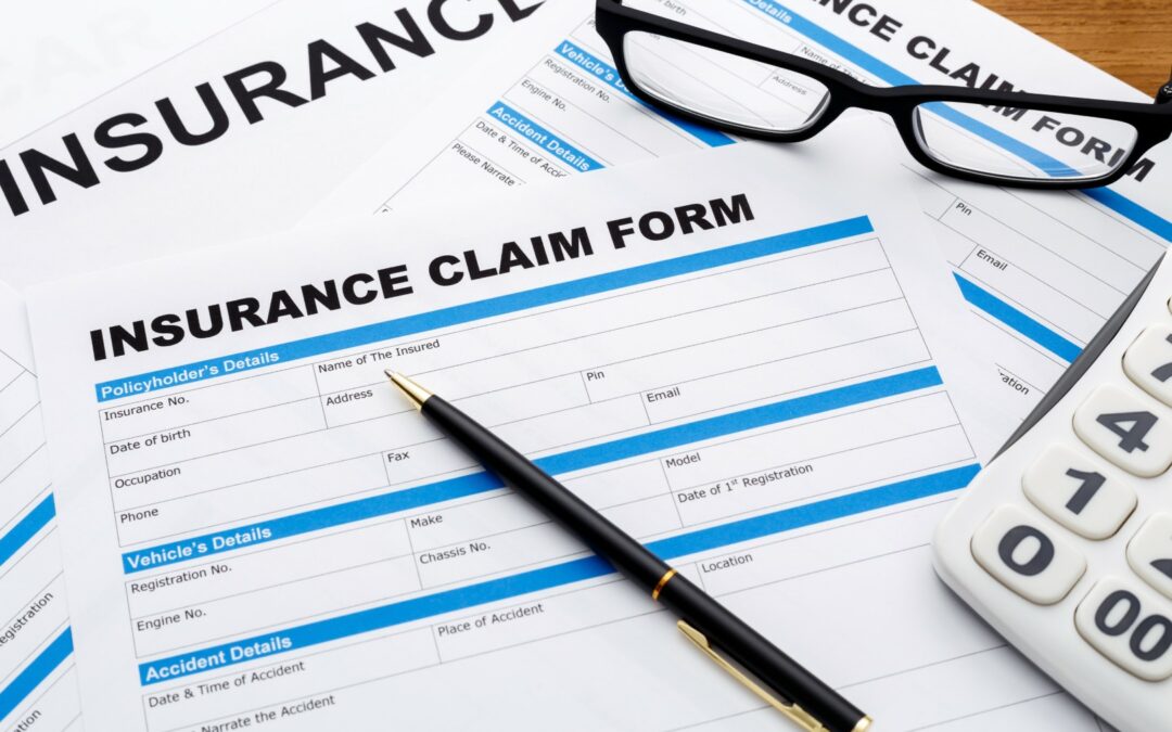 Insurance claim form with pen, calculator and glasses on wooden desk